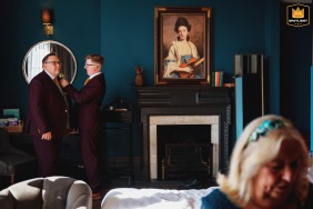 Groom receiving assistance in an elegant hotel room with rich turquoise teal walls, in Bristol, UK.
